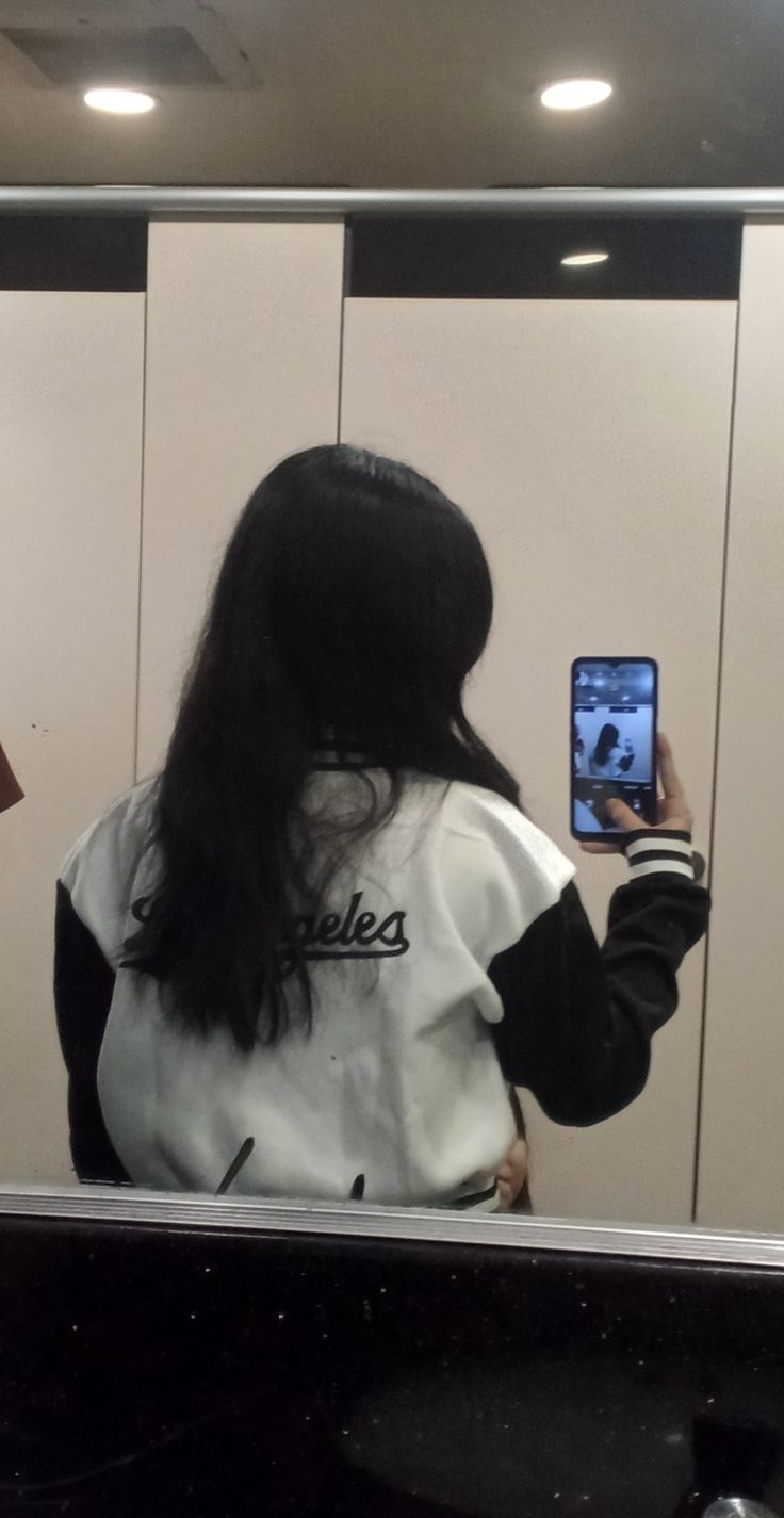 a woman is taking a selfie in the mirror with her cell phone while wearing a white and black jacket