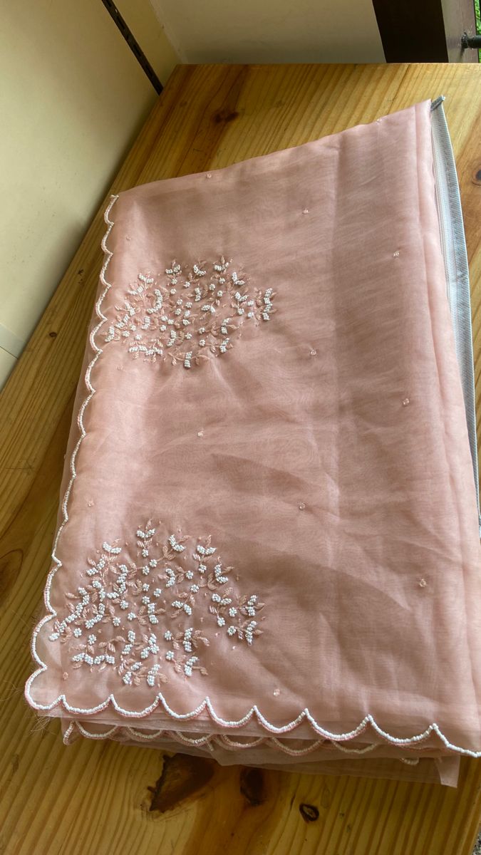 a pink table cloth with white embroidered flowers on it, sitting on a wooden surface