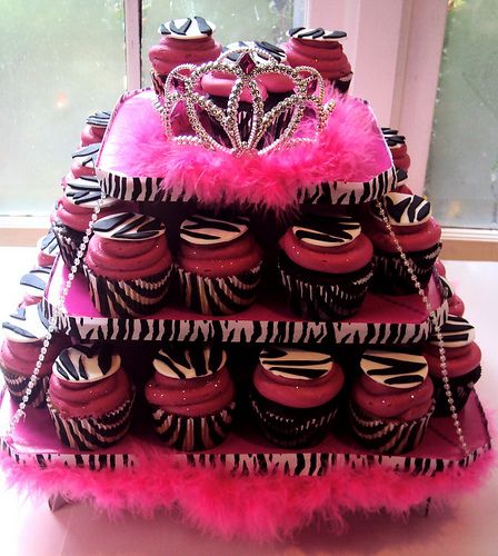 a cake made to look like a tower with cupcakes on it and pink feathers