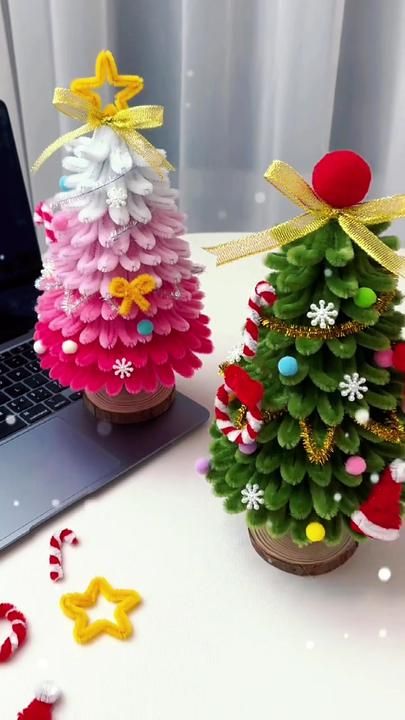 two small christmas trees sitting on top of a table next to an open laptop computer