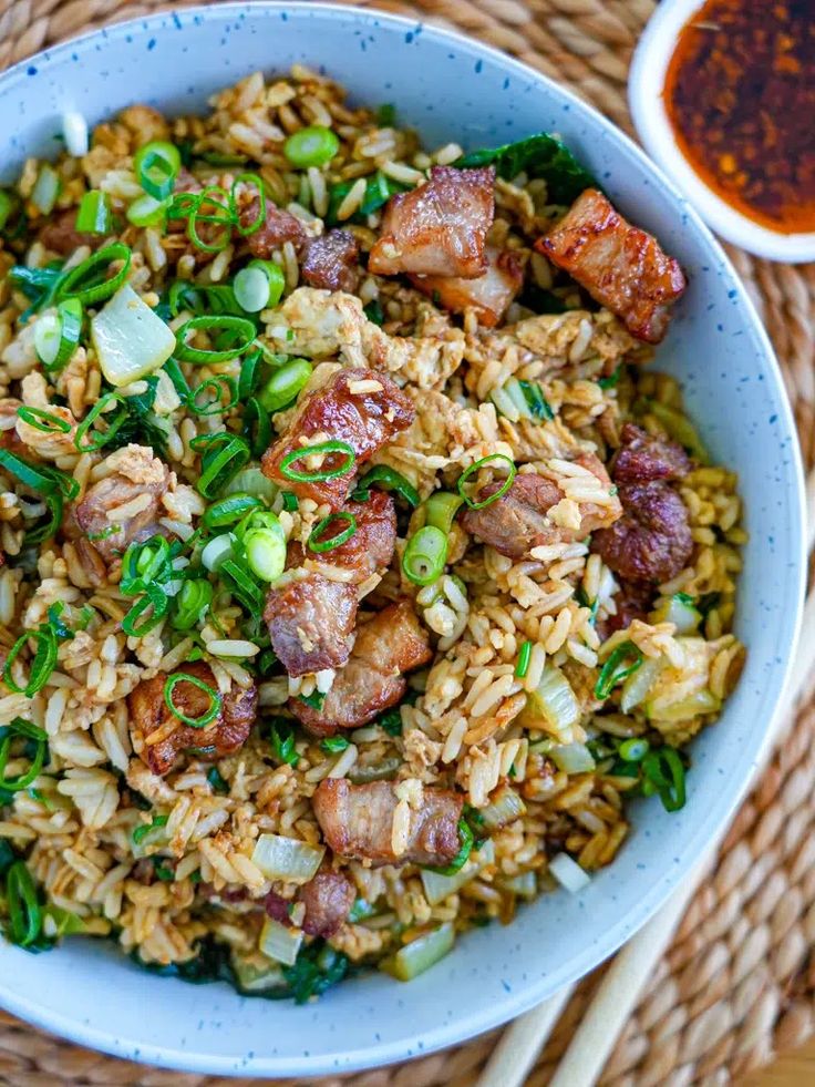 a bowl filled with rice and meat on top of a table next to chopsticks