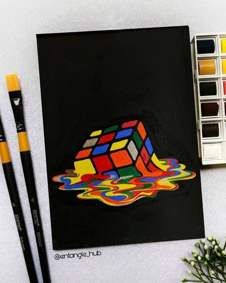 an art project with paint and watercolors on the table next to it is a rubix cube