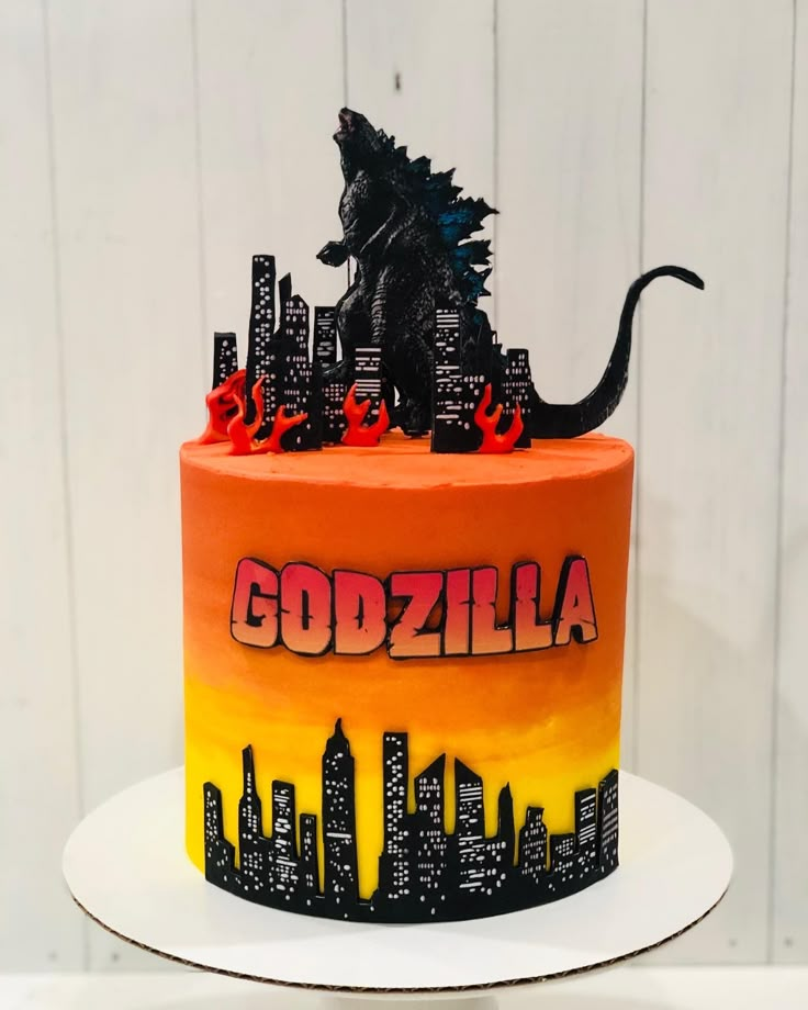 a godzilla themed birthday cake with city skylines in the background and red flames on top