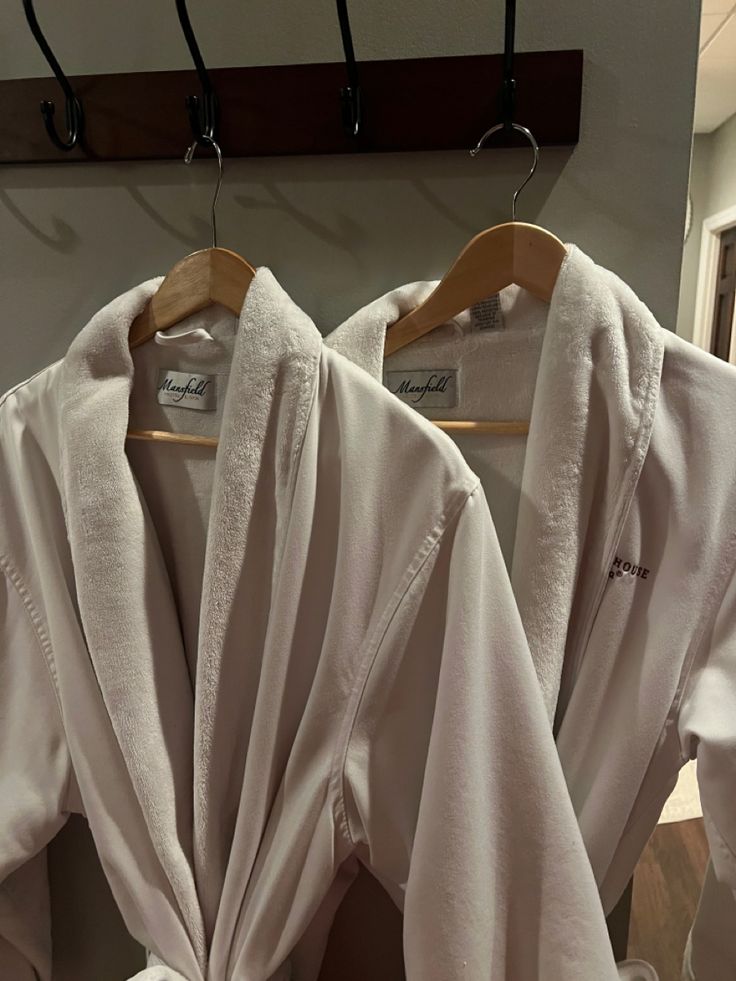 two robes are hanging on a rack in front of a mirror, one is white and the other is beige