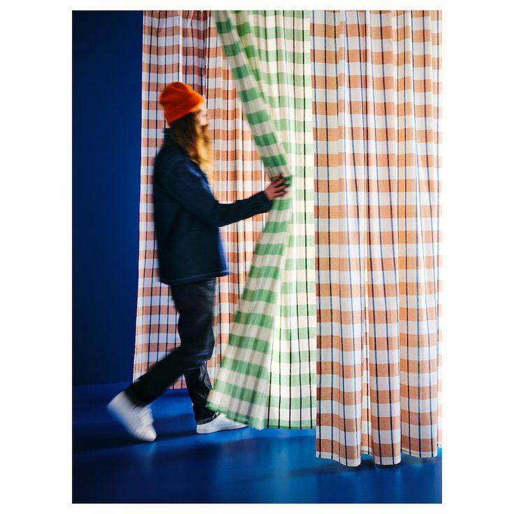 a person is walking by some curtains with orange and green stripes on them, while the man has his foot up against the curtain