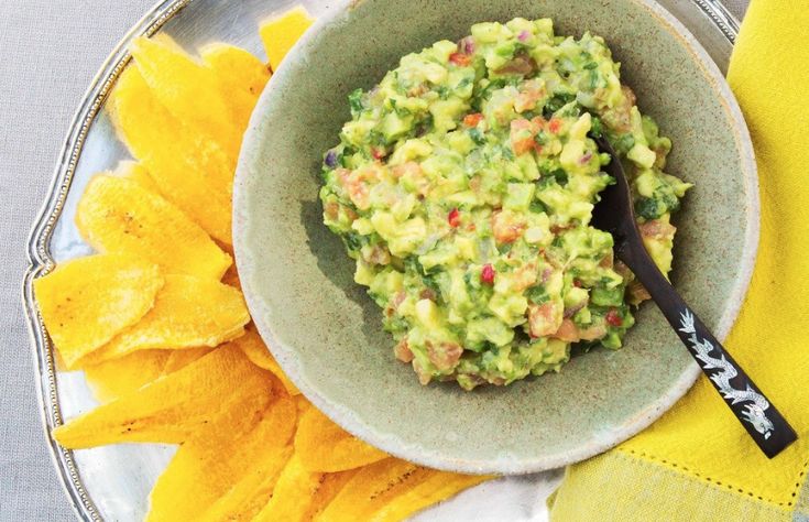 a bowl filled with guacamole on top of a table next to chips