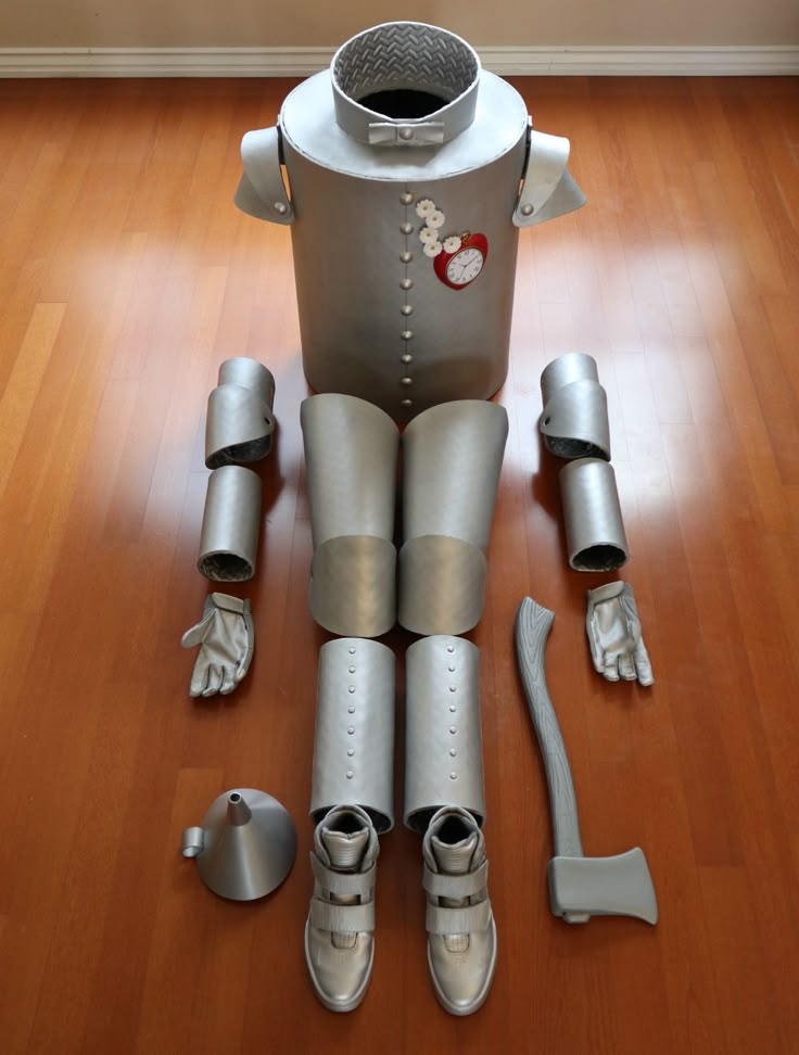 a robot sitting on top of a hard wood floor next to metal parts and tools