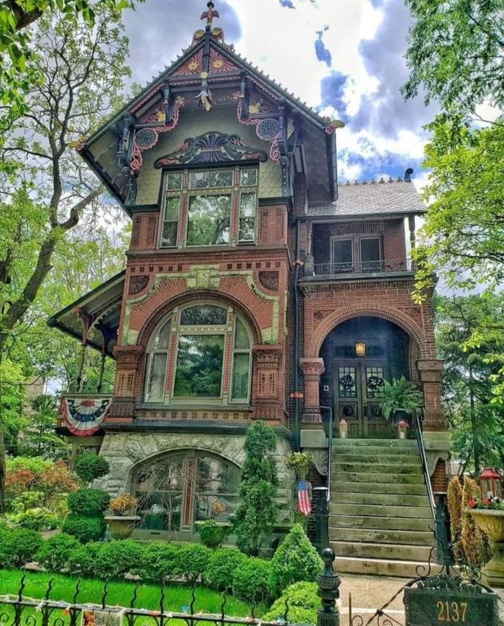 an old victorian house with many windows and steps leading up to the front door is surrounded by lush green trees