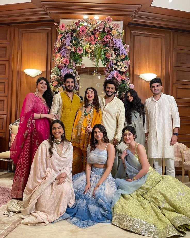 a group of people standing next to each other in front of a floral arrangement on the wall