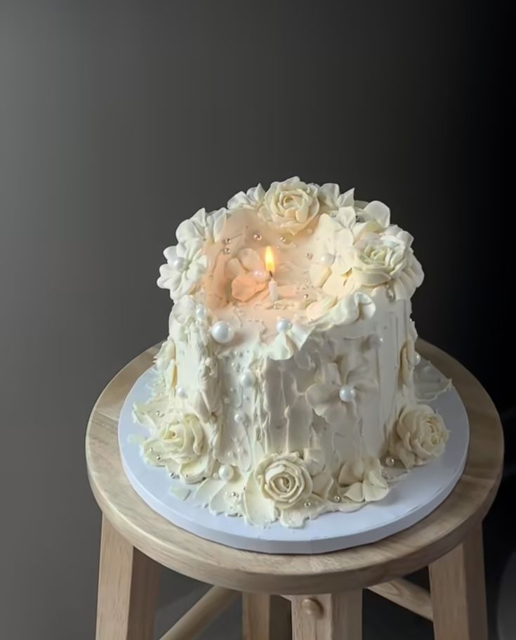 a white cake sitting on top of a wooden stool next to a lit candlestick