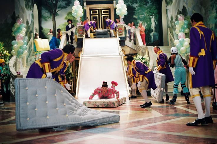 several people dressed in costumes standing around a fake mattress on the floor and another person laying down