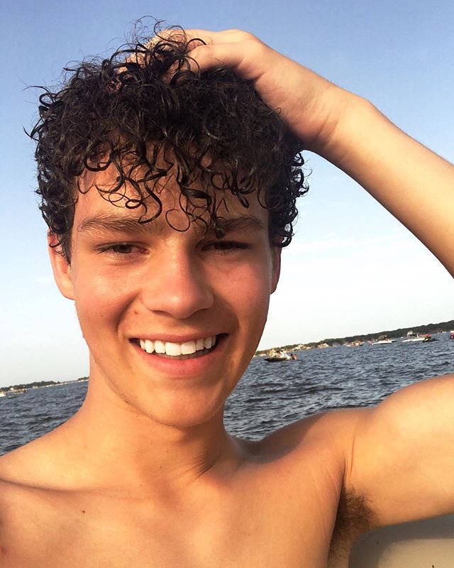 a man with curly hair is smiling while riding in a boat