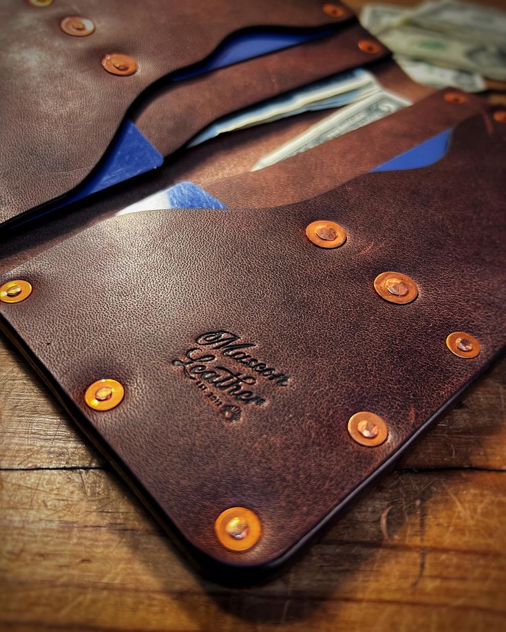 a leather wallet with buttons on it sitting on top of a wooden table next to money