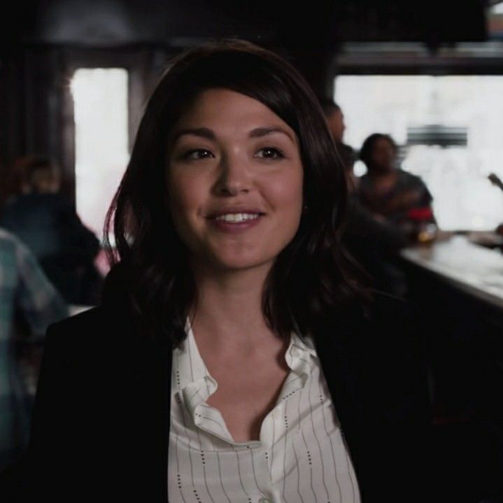 a woman standing in front of a bar smiling at the camera with other people behind her