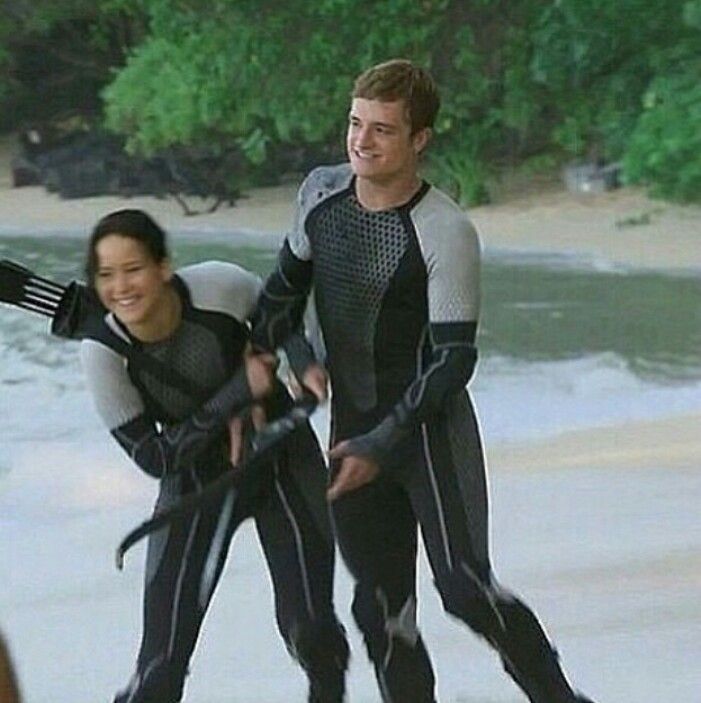 two people in wetsuits are holding paddles on the beach while another person watches