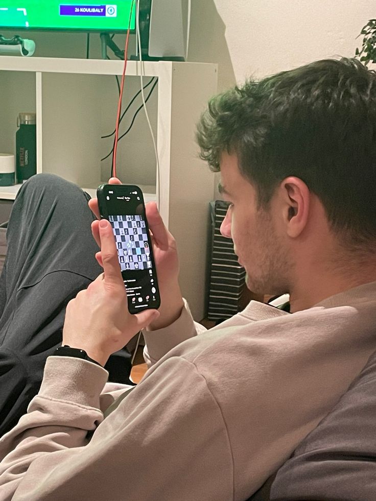 a man sitting on a couch holding up a cell phone to take a selfie