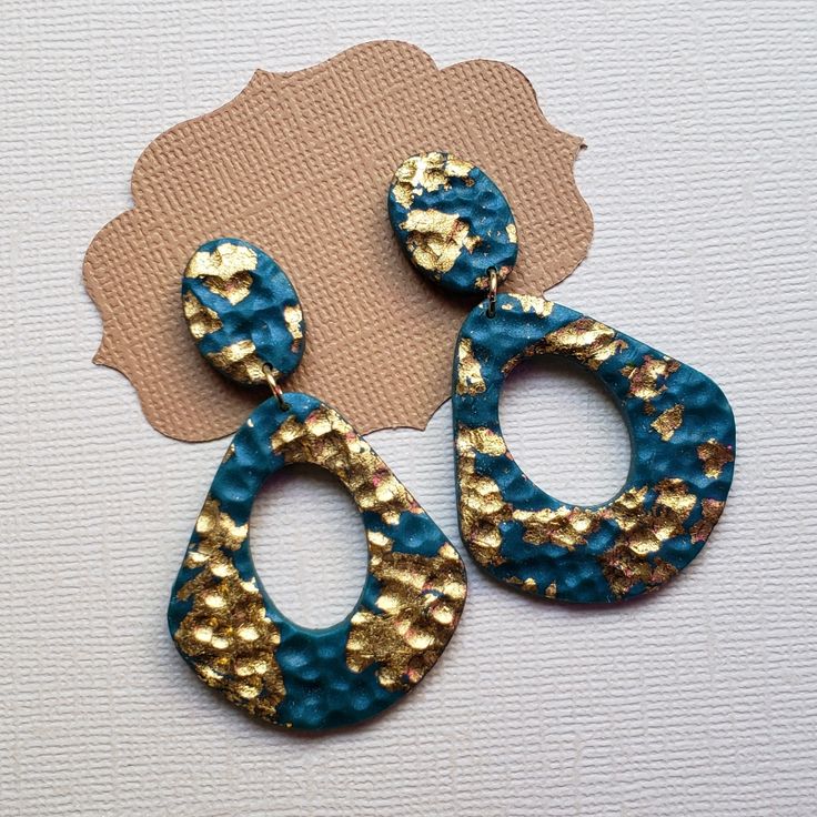 two pairs of blue and gold earrings on top of a white surface with a brown tag