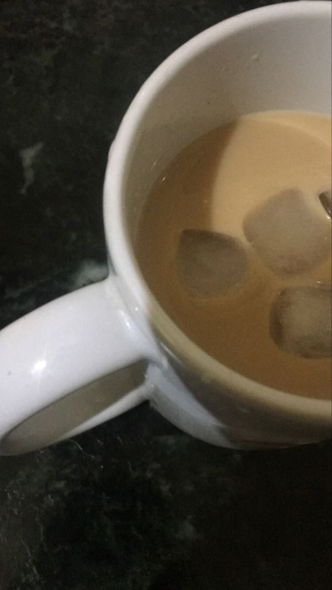 a cup filled with liquid and ice cubes on top of a black countertop