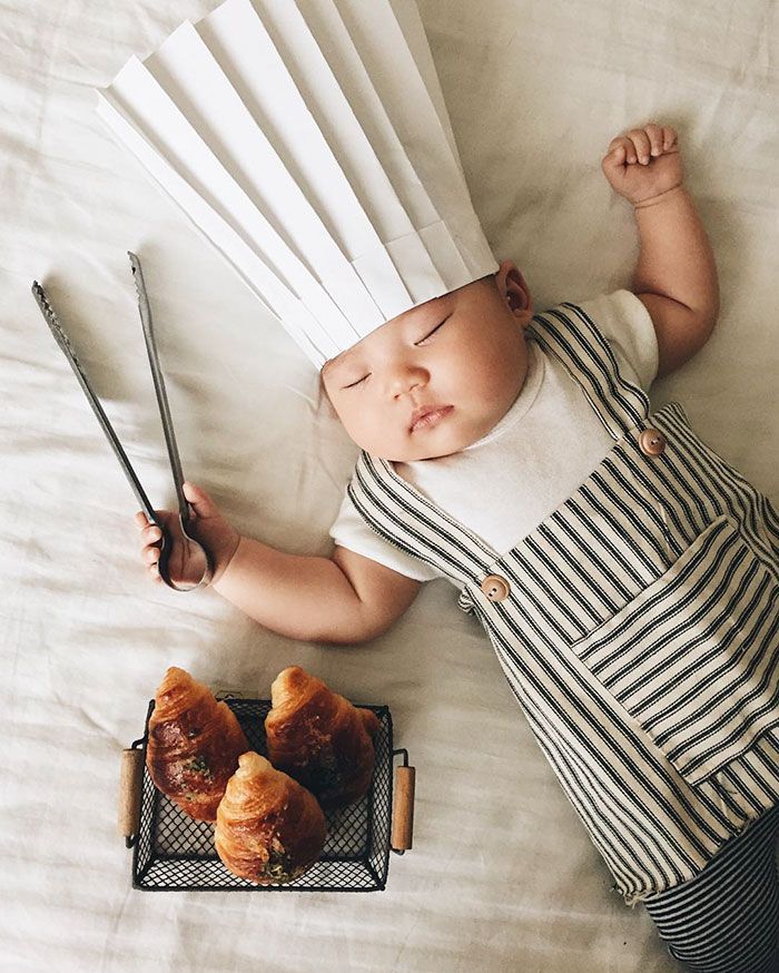 a baby laying on top of a bed wearing a chef's hat