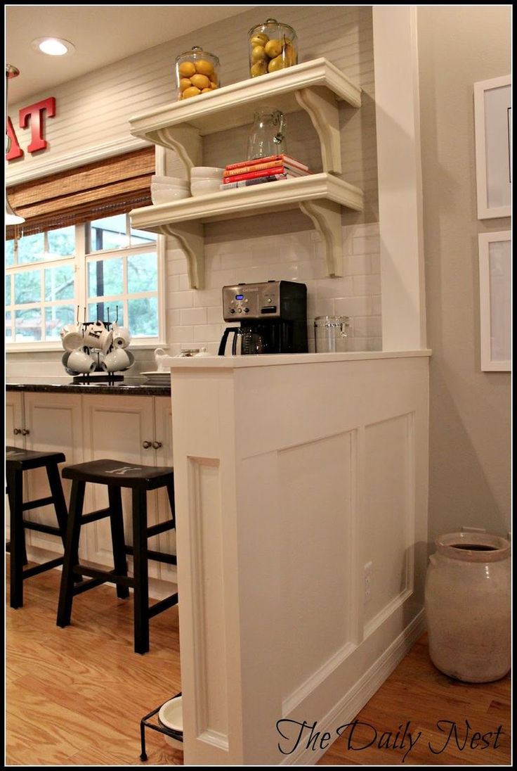 a kitchen with white cabinets and shelves filled with food on top of countertop next to bar stools