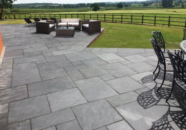 an outdoor patio with chairs and tables next to a large grassy field in the background