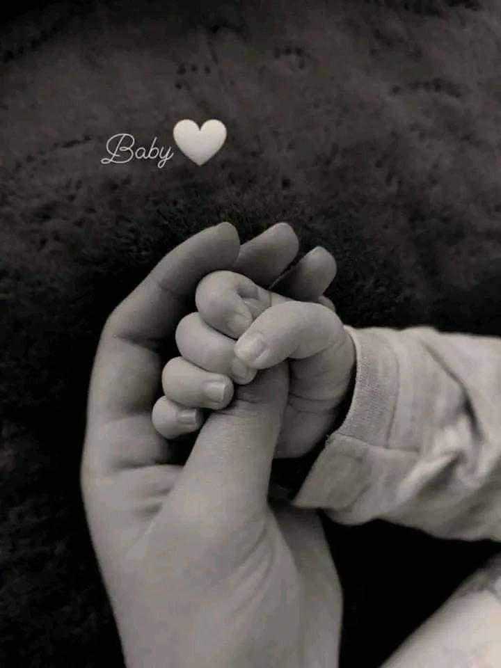 a black and white photo of a baby's hand holding the finger of his mother