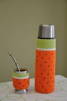 an orange and green crocheted water bottle next to a cup with a straw in it