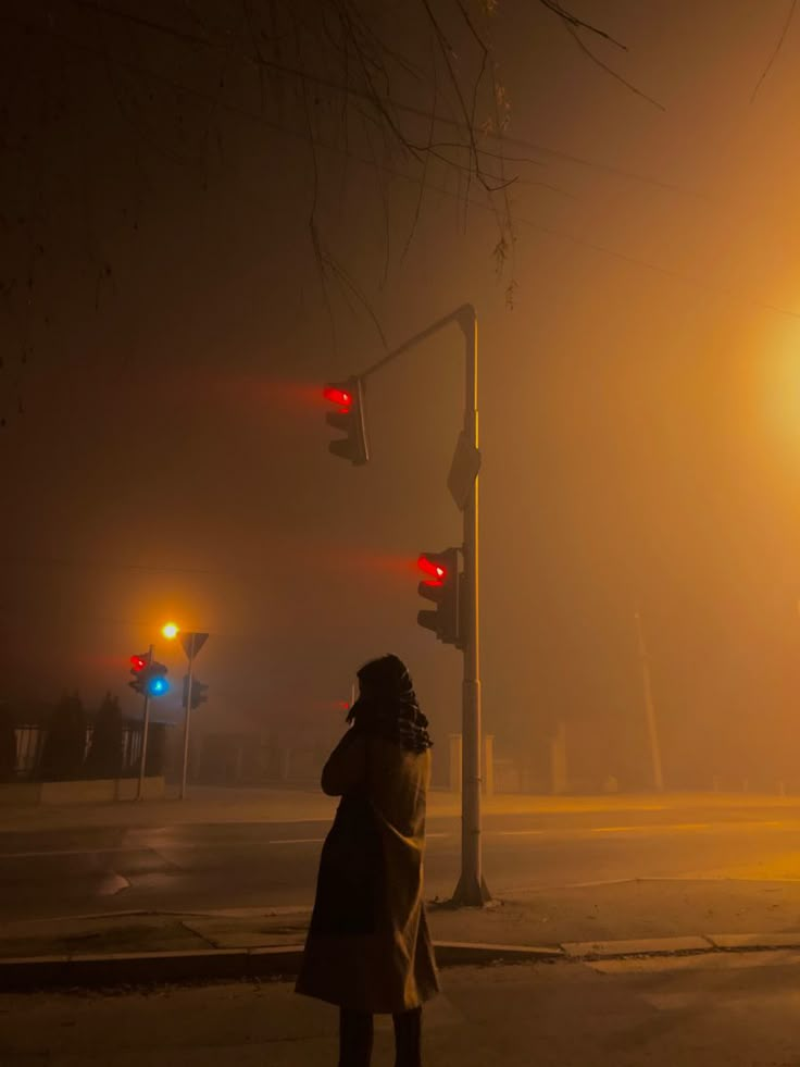 a woman is standing on the street at night talking on her cell phone and looking into the distance