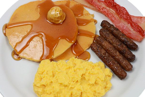 the breakfast plate has eggs, sausages, pancakes and bacon on it with syrup