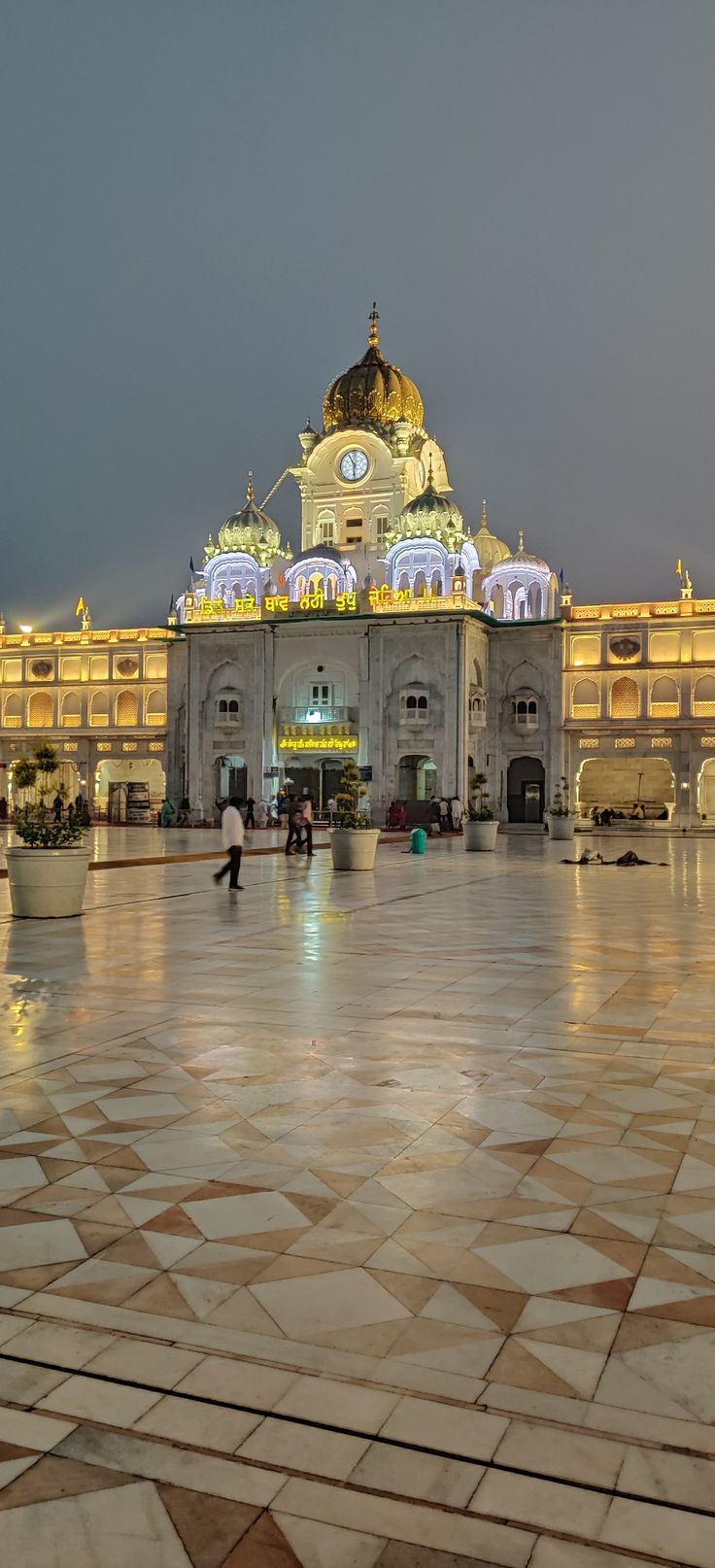 people are walking around in front of a large building with lights on it's sides