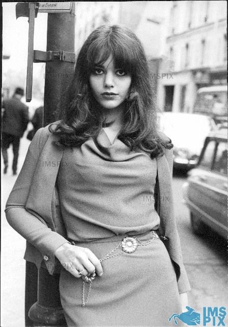 an old photo of a woman leaning on a pole with her hands in her pockets