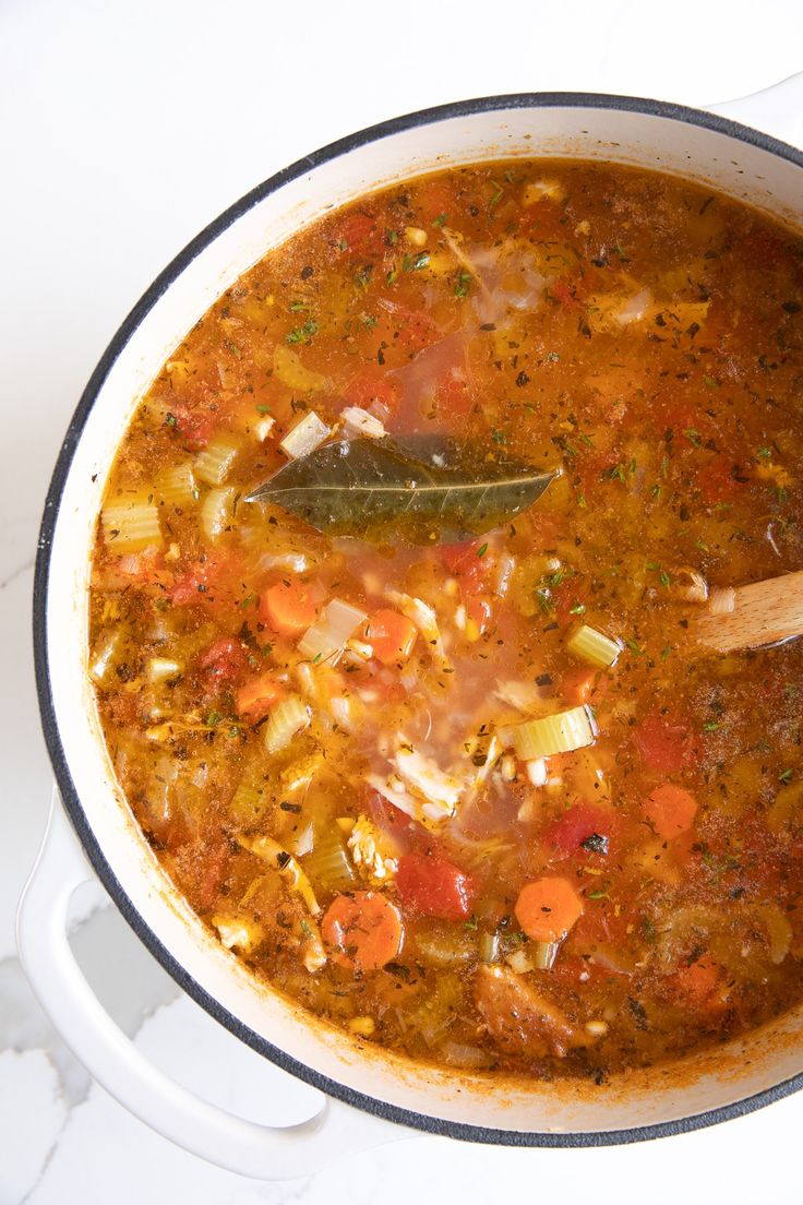 a pot filled with soup and vegetables on top of a white counter next to a wooden spoon