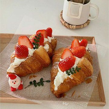 two croissants topped with strawberries and whipped cream on a tray next to a cup of coffee