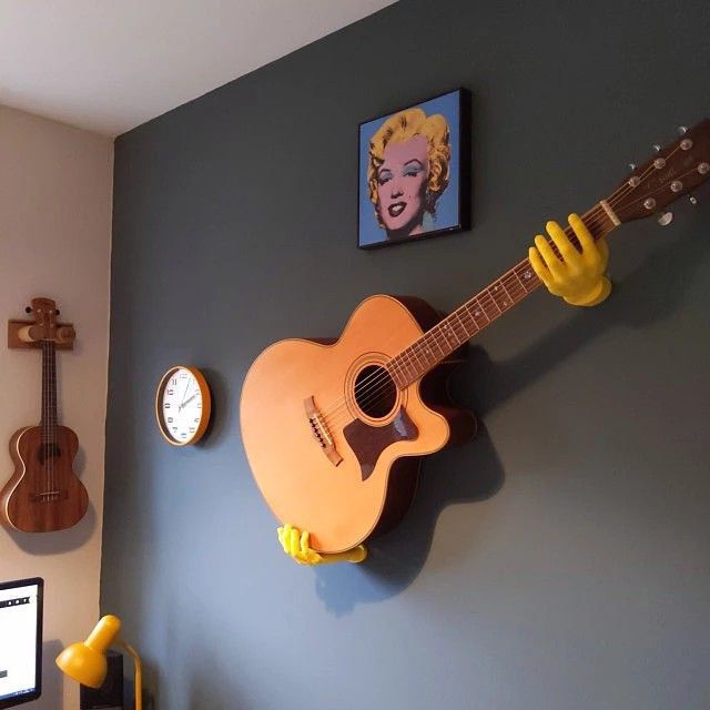 a guitar hanging on the wall next to a desk with a computer and other items