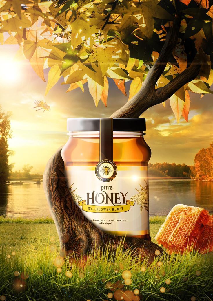 a jar of honey sitting in the grass next to a tree with leaves on it