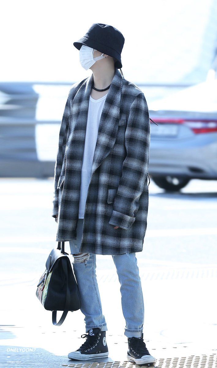 a man in plaid coat and black hat standing on sidewalk with handbag wearing face mask