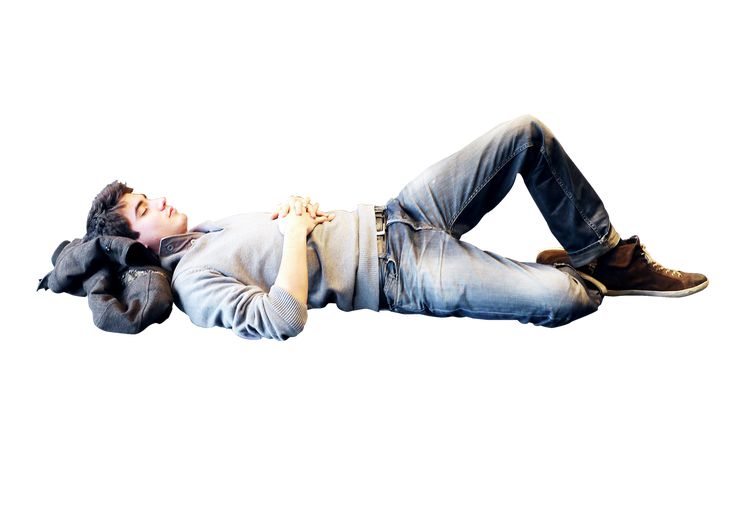 a young man laying on the ground with his hands in his pockets and head down