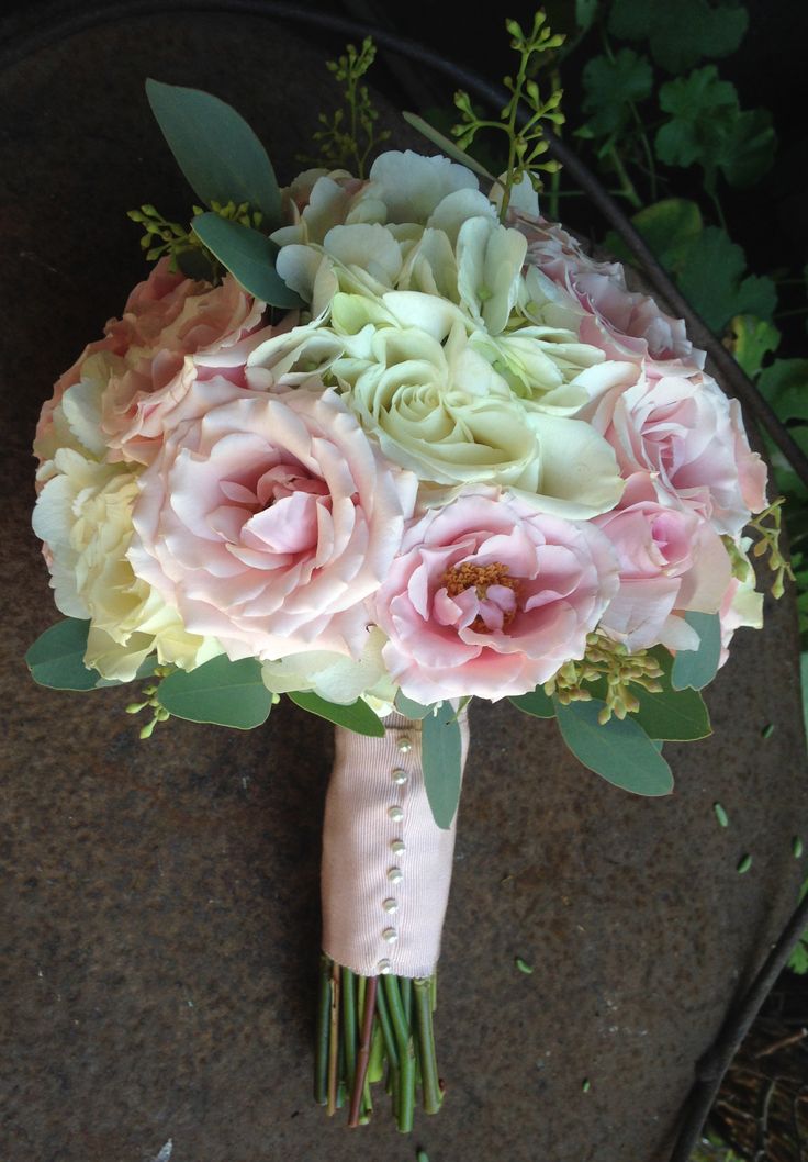 a bridal bouquet with pink flowers and greenery on the side of a stone wall