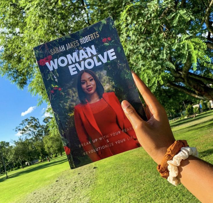 a woman is holding up a book in the park