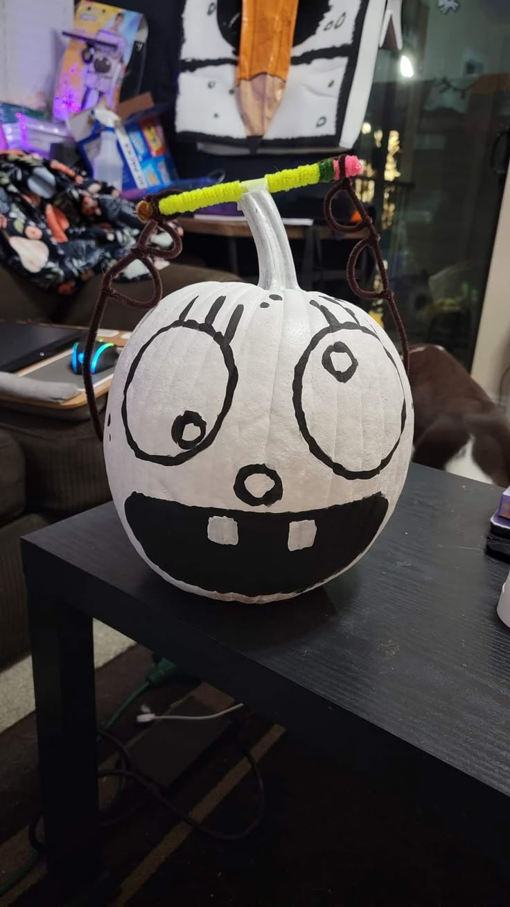 a white pumpkin decorated with black and white face drawn on it's side sitting on a table