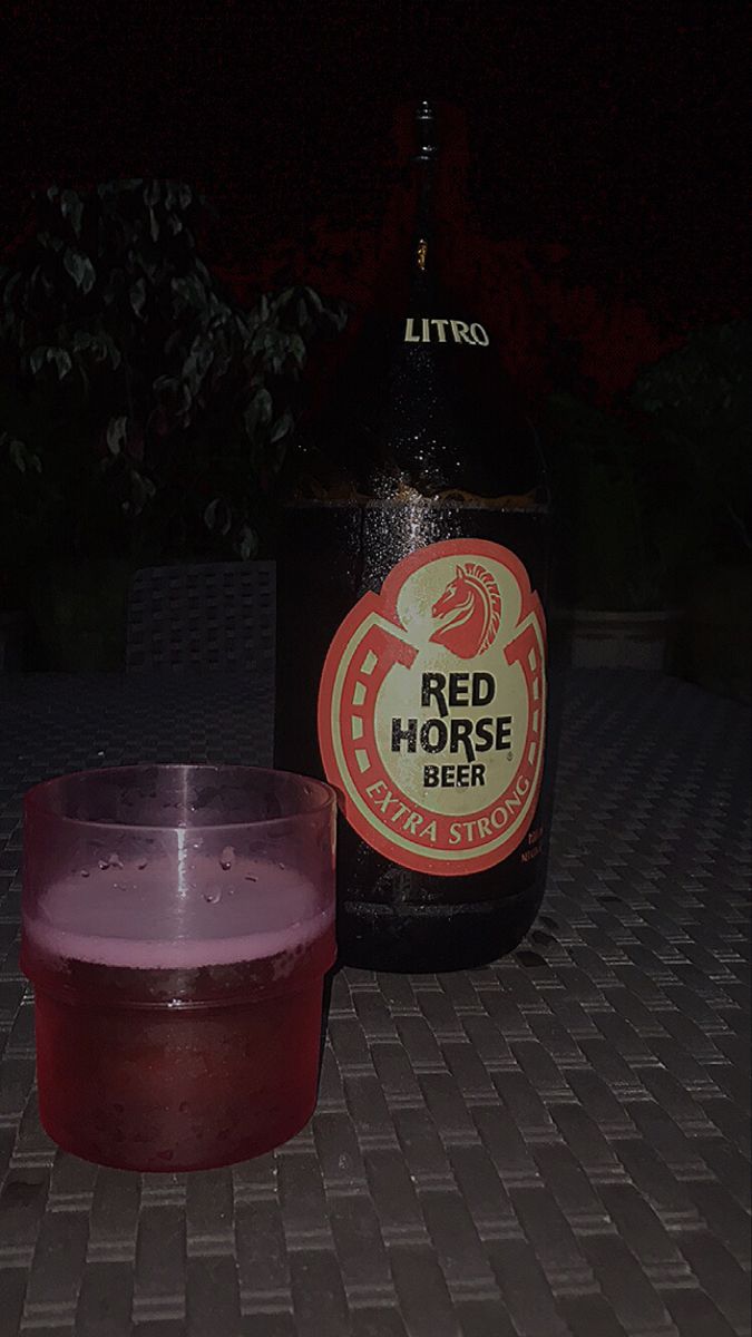 a bottle of red horse beer sitting next to a glass on a table outside at night