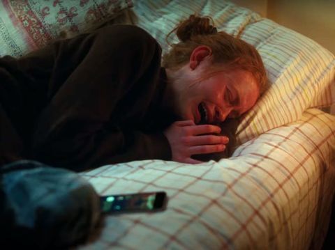 a woman laying in bed with her head on the pillow while holding a remote control