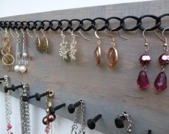 several pairs of earrings are hanging on a wall mounted jewelry rack with chains and hooks