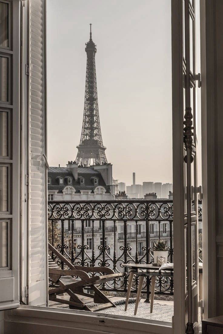 black and white photograph of the eiffel tower seen through an open window with chairs