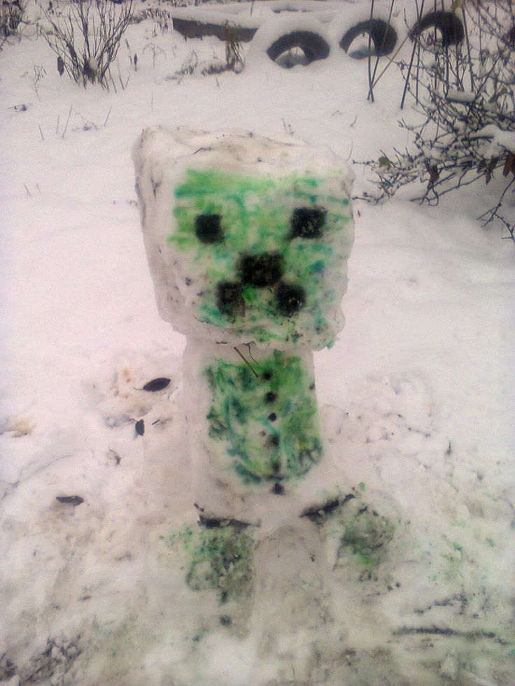 a snowman made out of green and black stuff in the snow with trees behind it