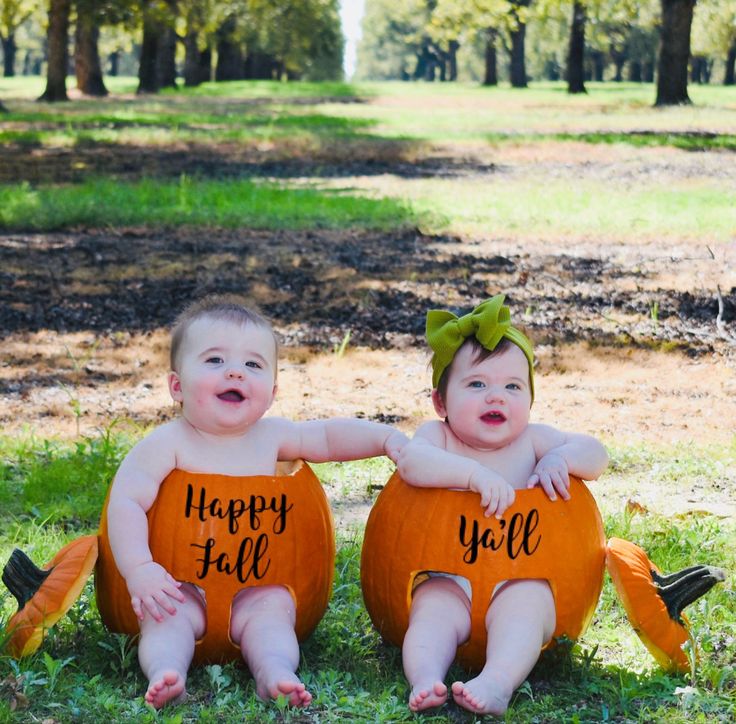 two babies sitting on pumpkins in the grass with happy fall written on their backs