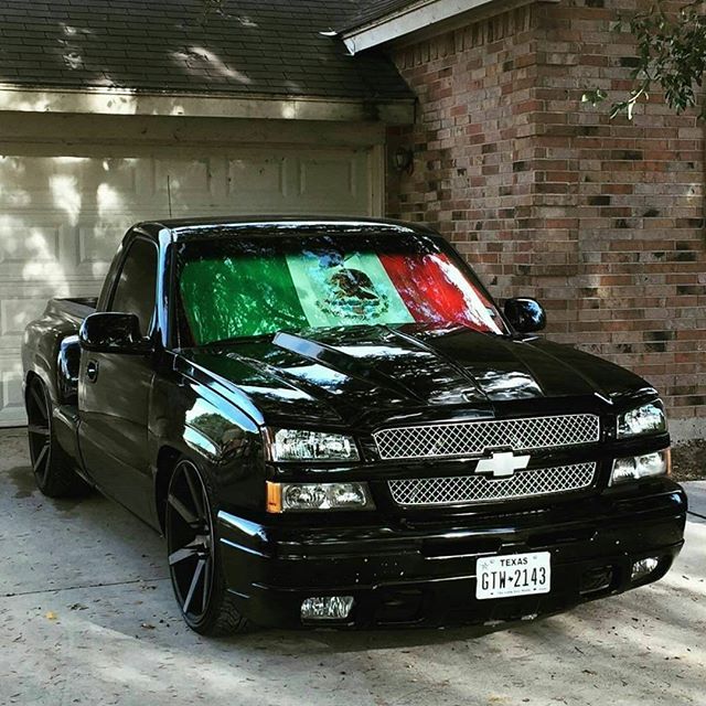 a black truck parked in front of a house with a mexican flag on the hood