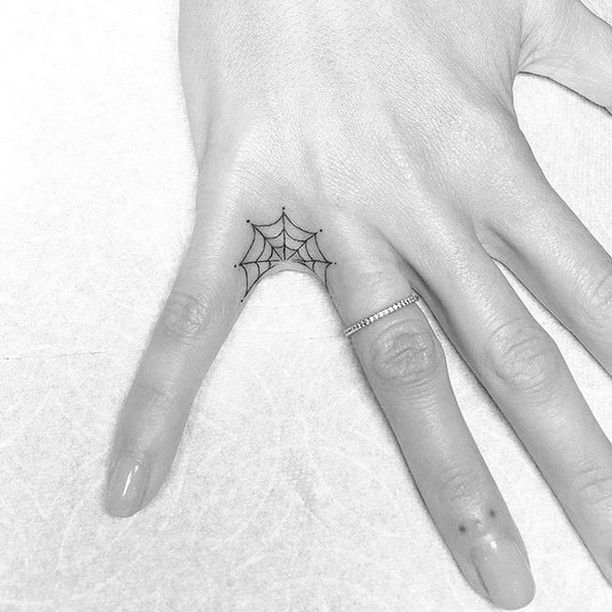 a person's hand with a spider web tattoo on the middle of their finger