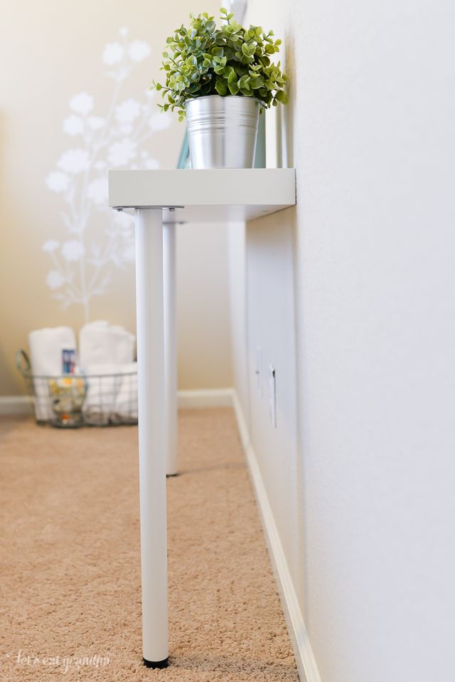 a white table with a potted plant sitting on it's side next to a wall