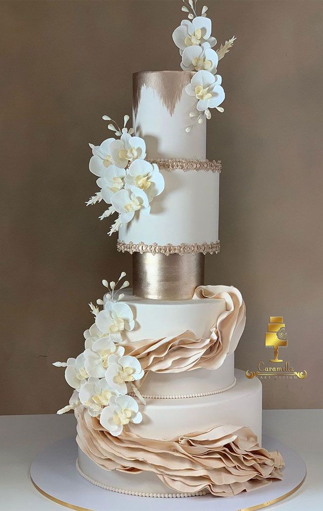 a three tiered wedding cake with white flowers on top and gold trimmings